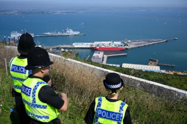 PORTLAND, ENGLAND - AUGUST 10: Police officers look out over the Bibby Stockholm immigration barge, at Portland Port, on August 10, 2023 in Portland, England. The first residents arrived on August 7th as the British government seeks to relocate asylum seekers from government-leased hotels. The Home Office says the vessel can accommodate up to 500 migrants and rejected criticism that the facility is unsafe. (Photo by Finnbarr Webster/Getty Images)