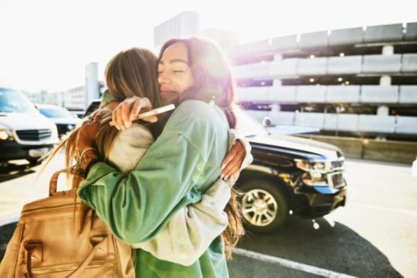 Medium shot of two women hugging curbside at airport