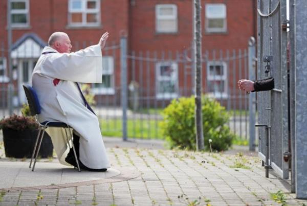 Fr Paddy McCafferty resumes hearing co<em></em>nfessions while observing social distancing though the locked gates of Corpus Christi Church in Ballymurphy, West Belfast. PA Photo. Picture date: Saturday May 2, 2020. See PA story HEALTH Coro<em></em>navirus Ulster. Photo credit should read: Niall Carson/PA Wire